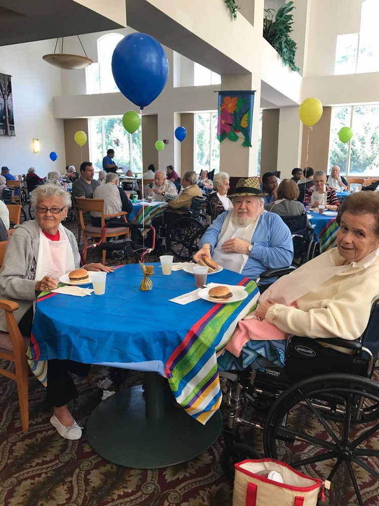 A group of seniors enjoying a community event inside a hall, adorned with colorful balloons and decorated tables.