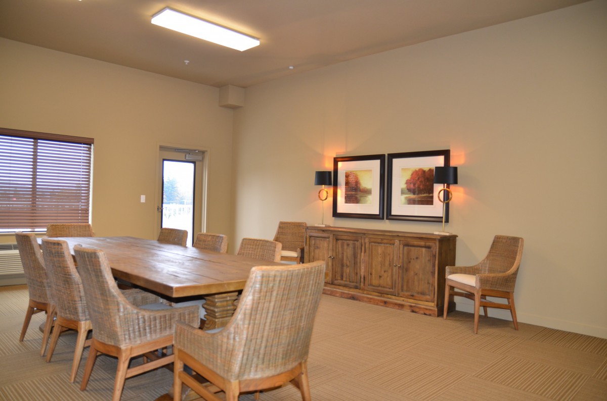 A dining room with a wooden table, several chairs, and framed artwork on the wall.