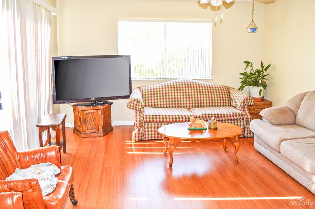 A cozy living room with a checkered sofa, wooden flooring, and a large television.