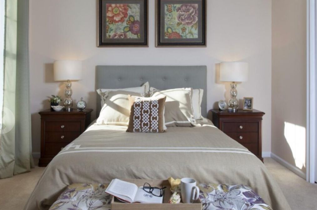 A cozy bedroom scene featuring a neatly made bed with decorative pillows, flanked by wooden nightstands and elegant lamps, with framed artwork on the wall.