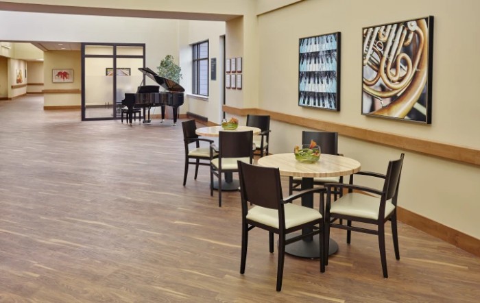 A modern lobby with tables and chairs, featuring artwork on the walls and a grand piano in the corner.
