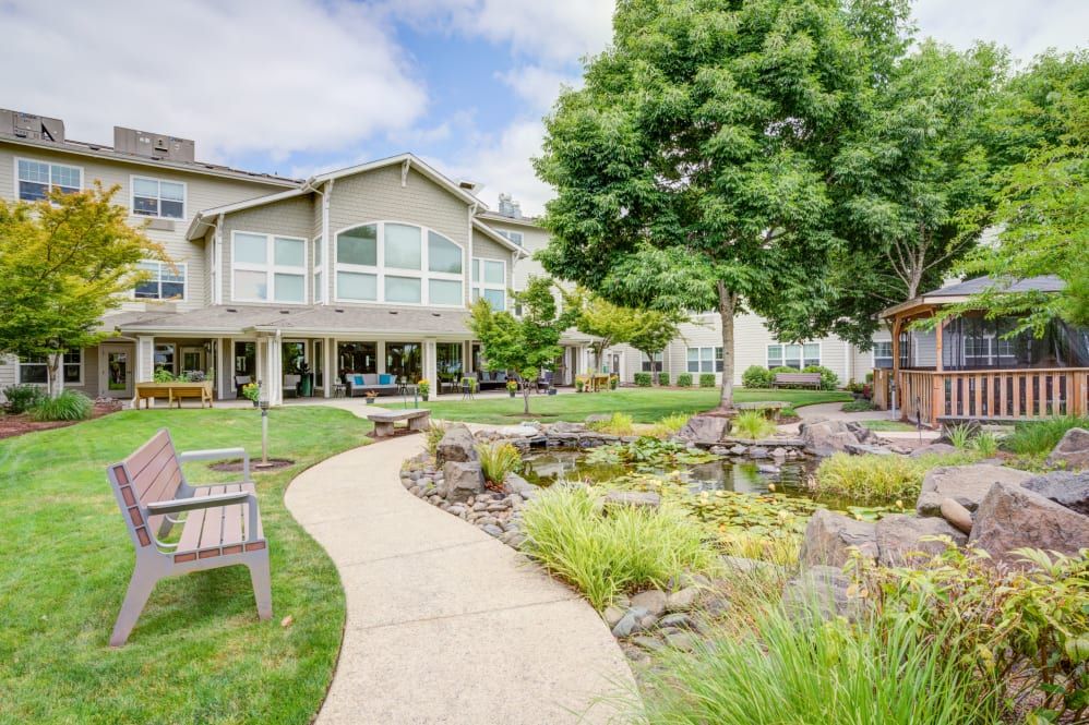 A serene garden with a winding pathway, benches, and a pond in front of a residential building.