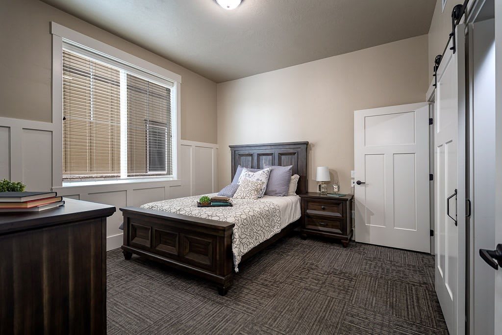 A cozy bedroom featuring a wooden bed and nightstand, with a large window allowing natural light.