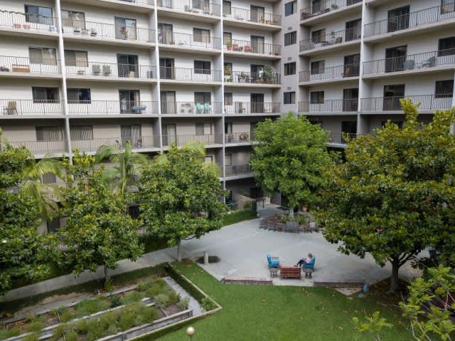 A view of an apartment building with a lush courtyard featuring trees and outdoor seating.