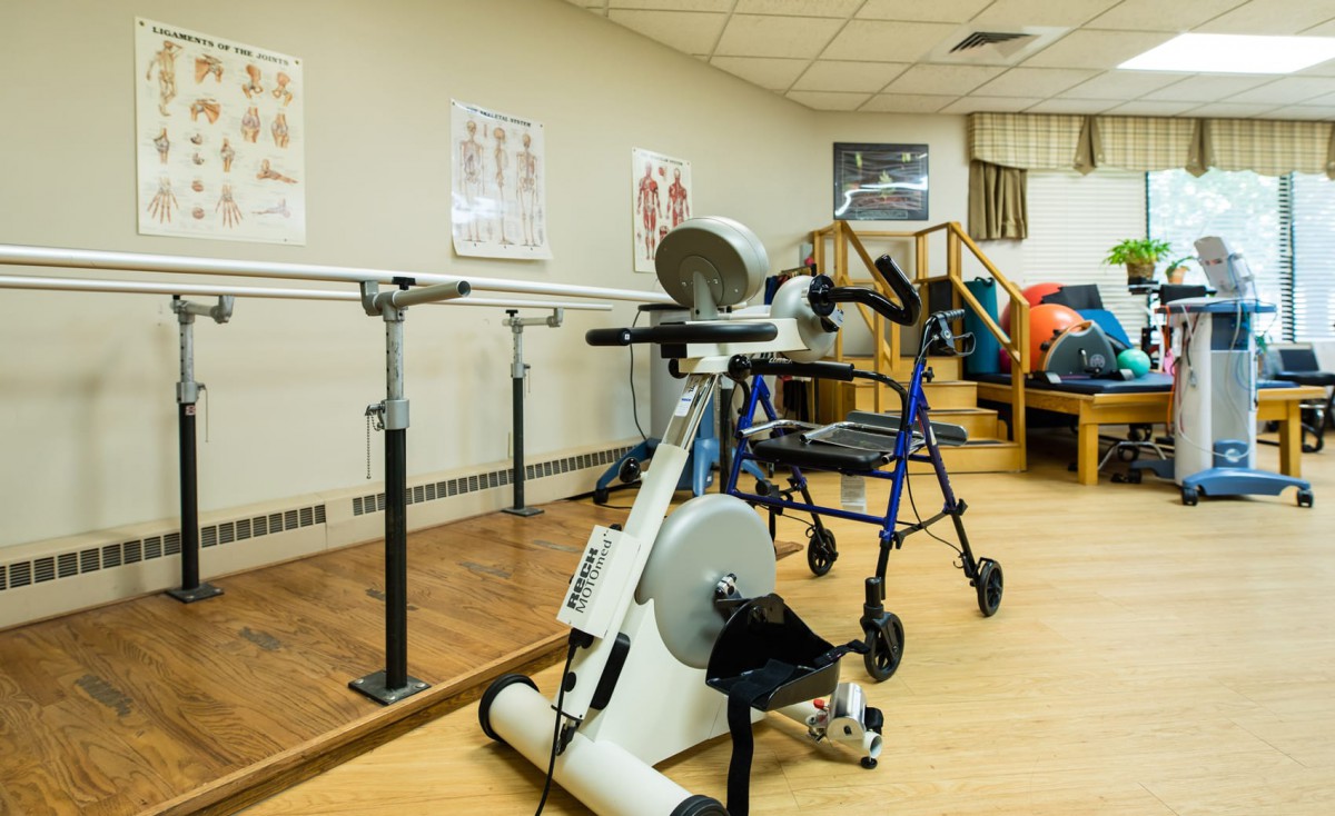 A rehabilitation room equipped with exercise machines and parallel bars for physical therapy.