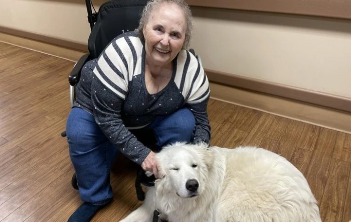 A smiling woman sitting beside a large white dog indoors.