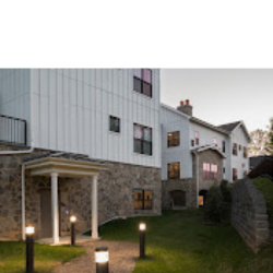 A modern residential building showcasing a blend of stone and siding with outdoor lighting along the pathway.
