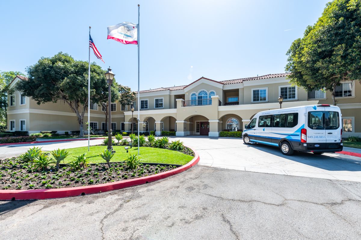 A sunny view of a building with flags, a van parked in front, and a landscaped area.