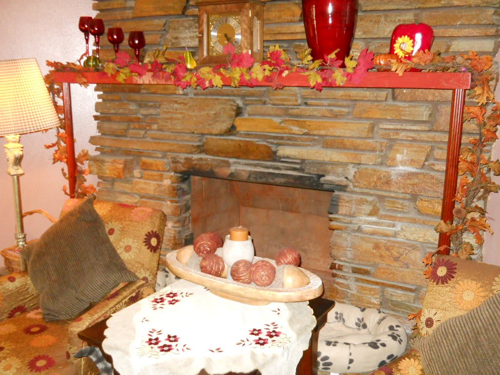 A cozy autumn-themed fireplace with rustic stonework, featuring candles and decorative leaves.