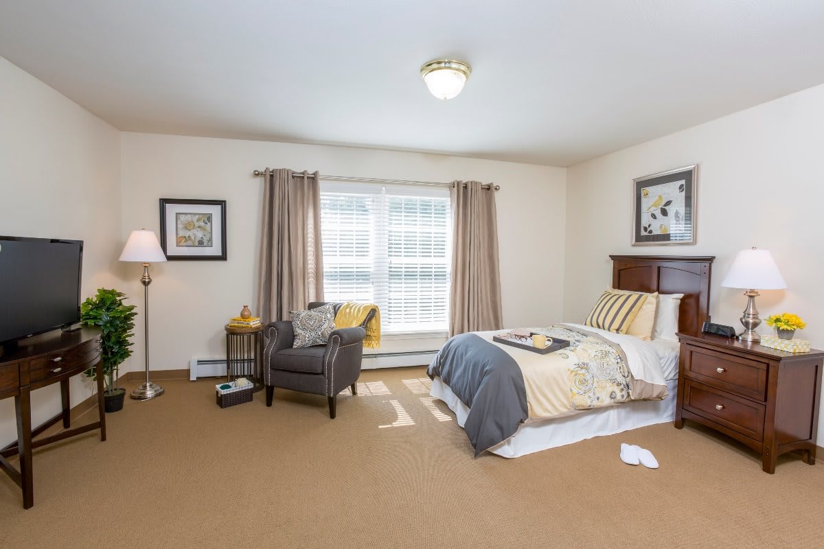 A cozy and well-furnished bedroom with a bed, armchair, and natural lighting.