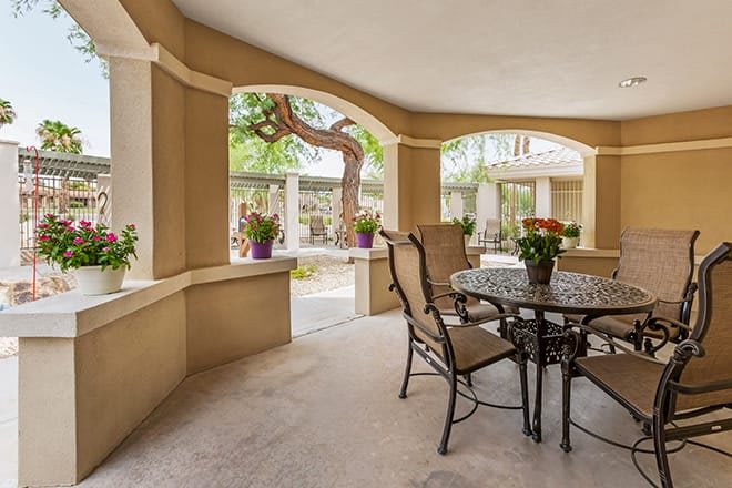 A cozy patio with a table and chairs, surrounded by plants in a covered outdoor area.