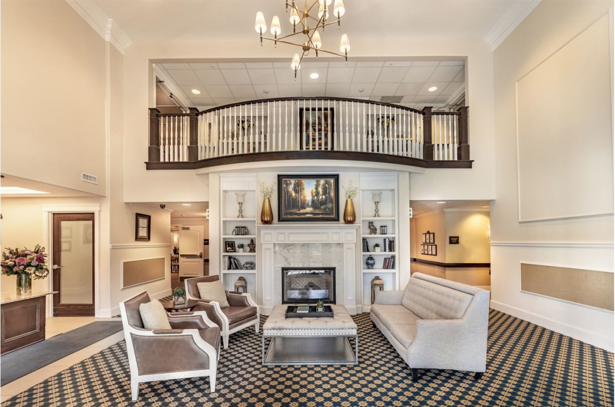 Elegant living room with a chandelier and balcony overlooking a seating area surrounding a fireplace.