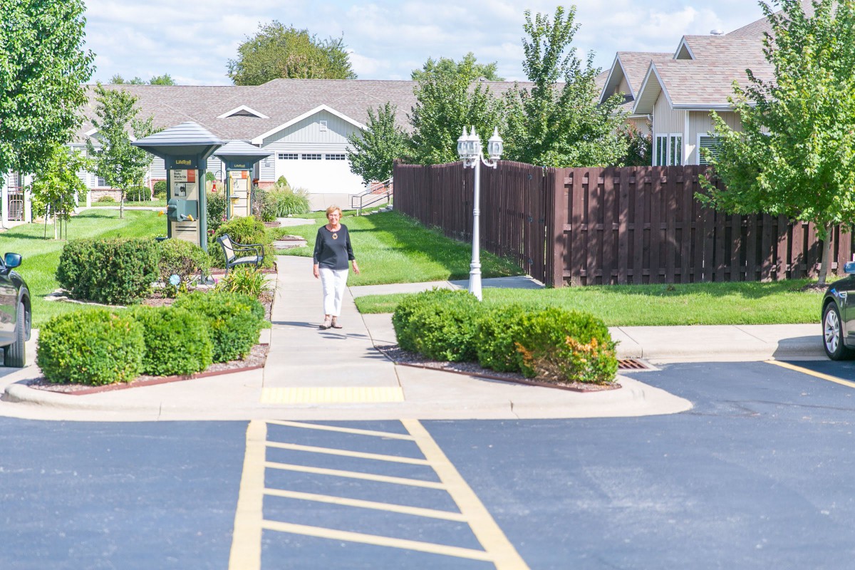 A serene suburban neighborhood with well-maintained landscaping and a person walking on the sidewalk.