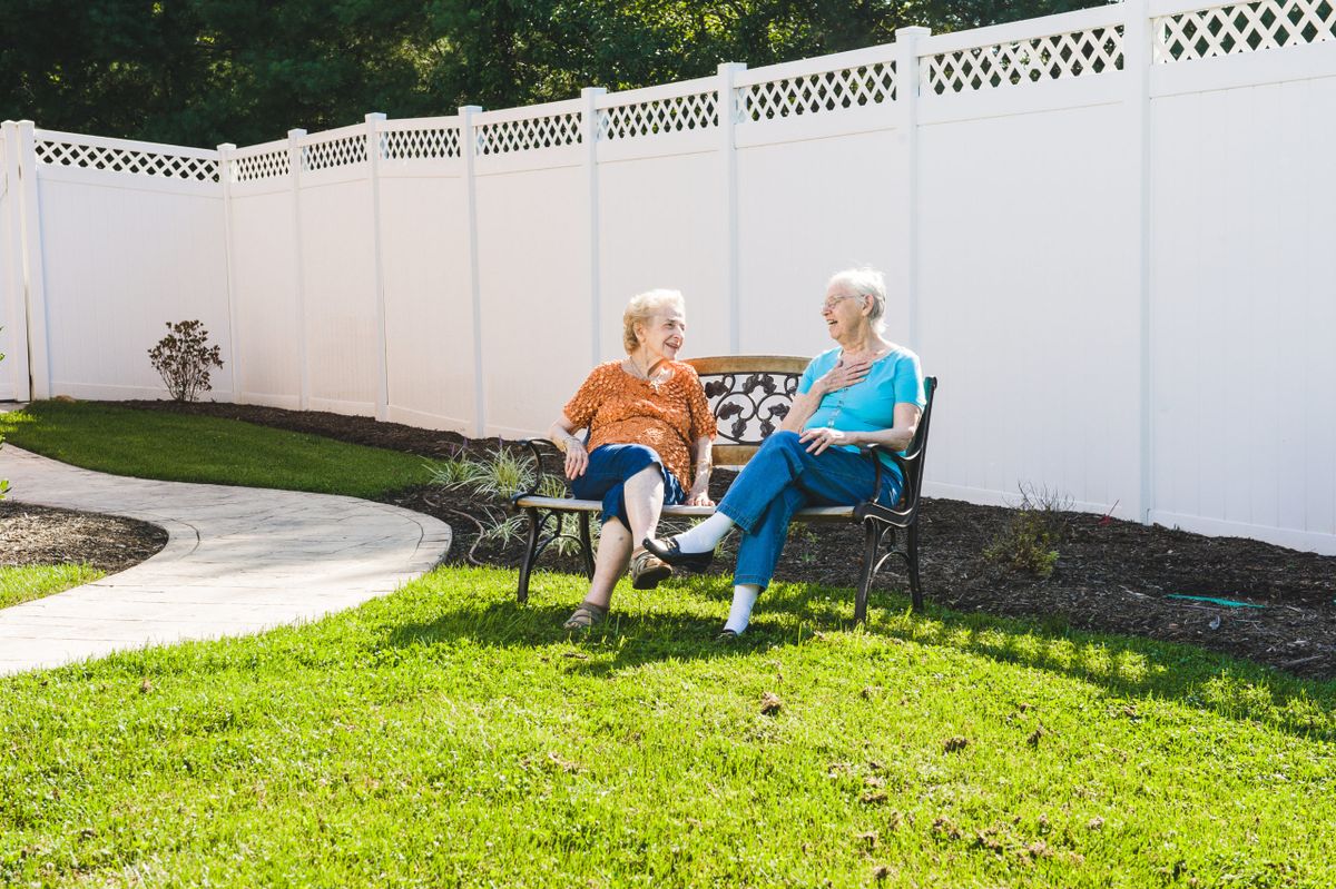 Two elderly women sitting on a bench, enjoying a conversation in a sunny garden.