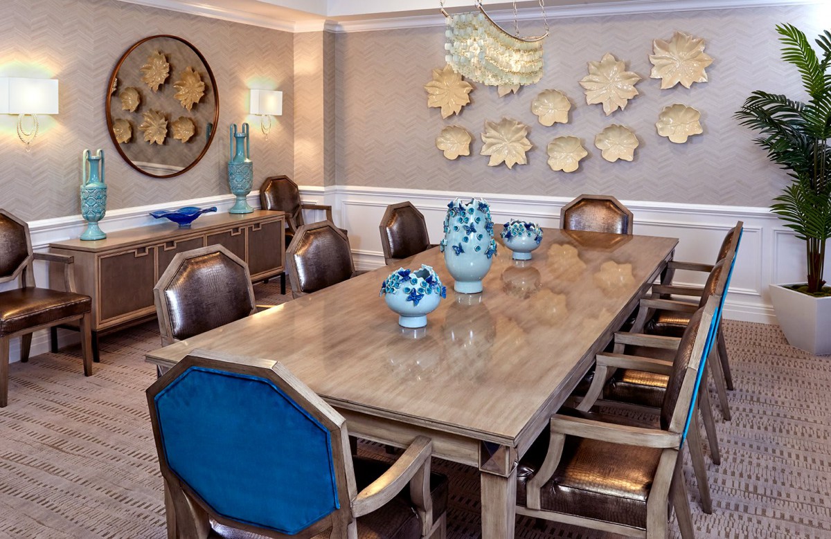 A stylish dining room featuring a large wooden table with blue-backed chairs, decorative vases, and wall art.