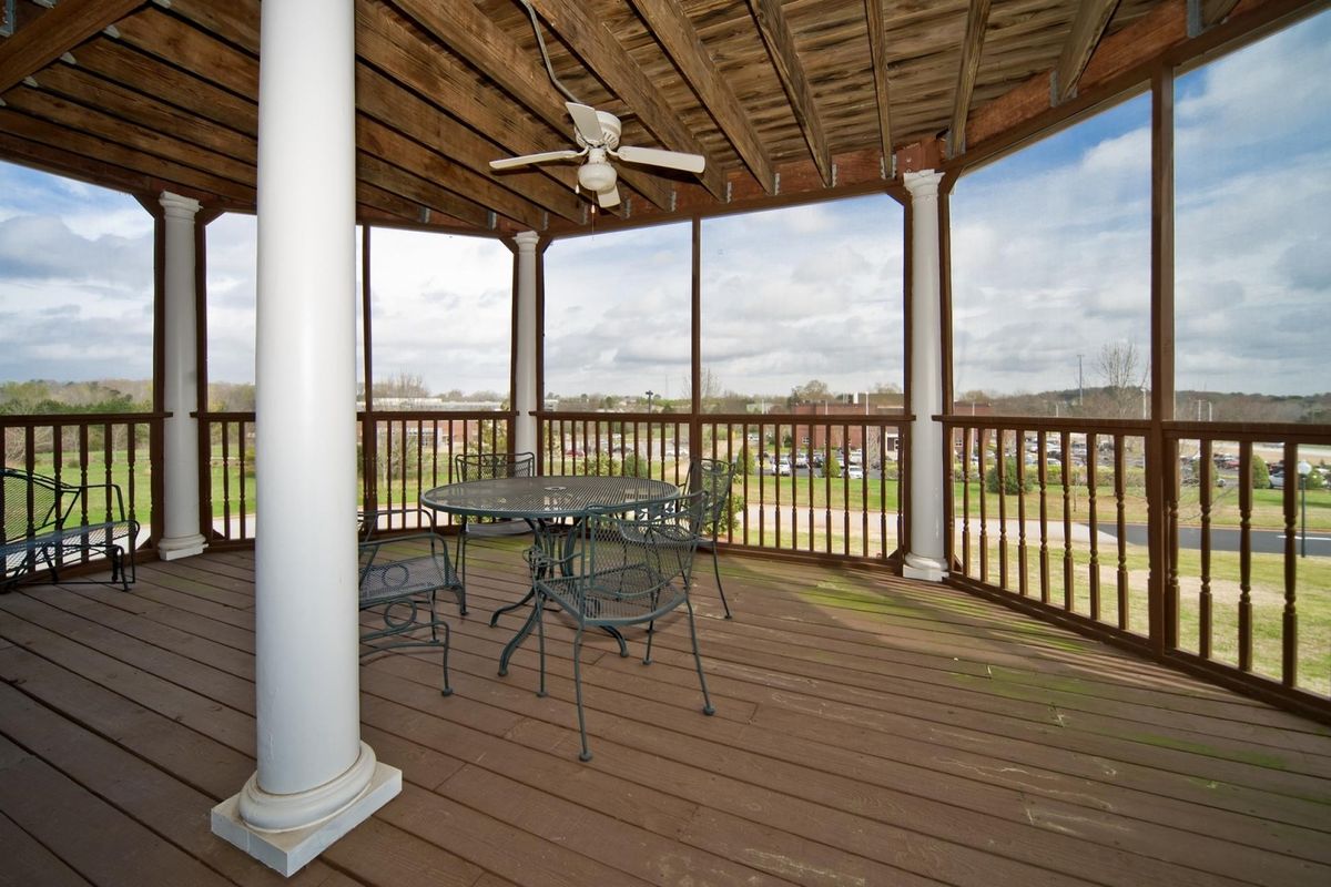 An outdoor patio with a ceiling fan, table, and chairs, surrounded by railings and columns.