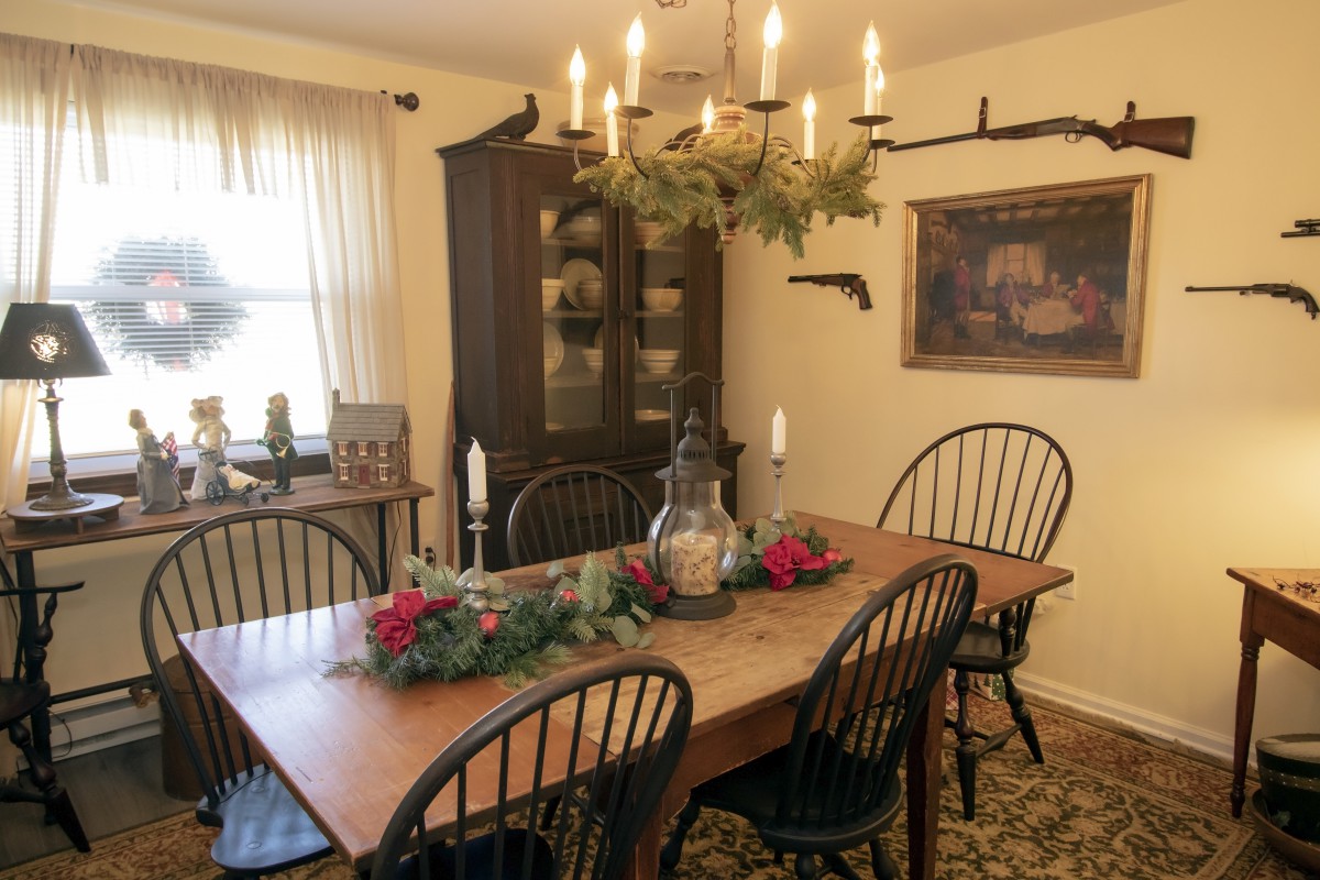 A cozy dining room with a wooden table, surrounded by chairs and decorated with greenery and candles under a rustic chandelier.