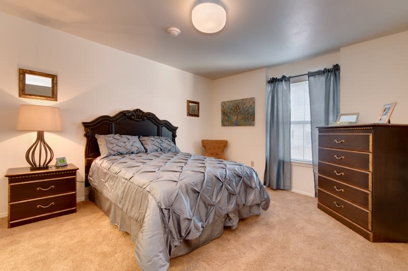 A cozy bedroom with a neatly made bed, a dresser, and drapes covering a window.