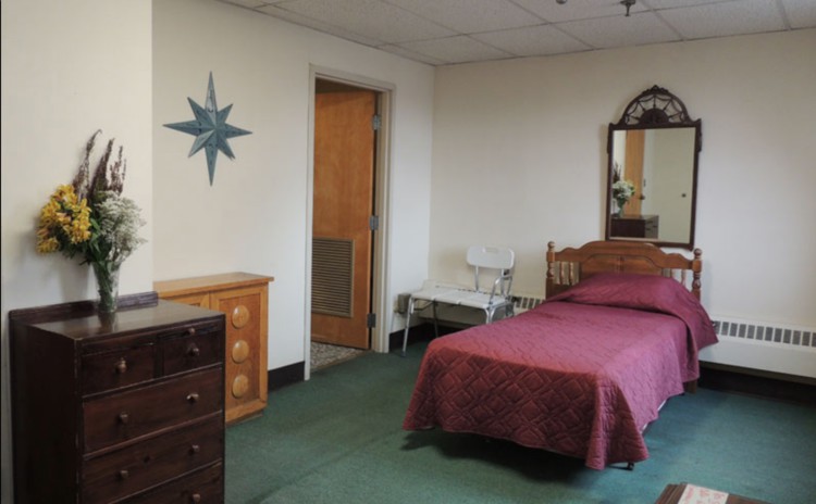 A modestly furnished bedroom featuring a single bed, dresser, and mirror.