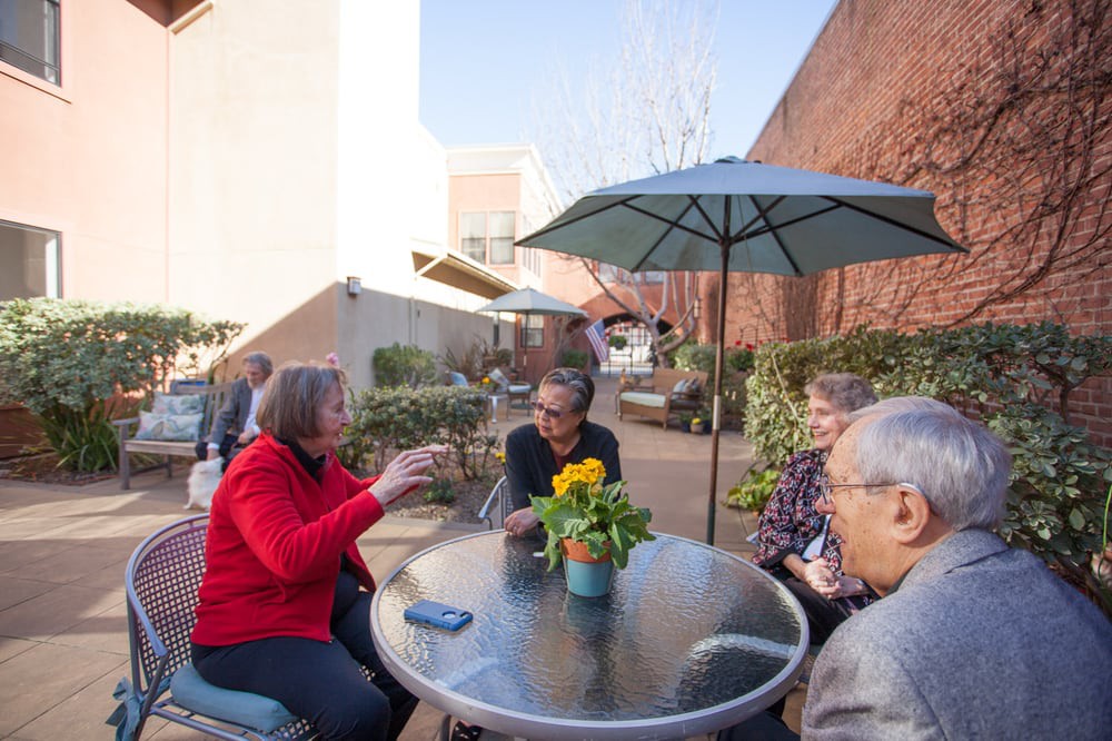A group of people sitting around a table outside, enjoying conversation on a sunny patio.