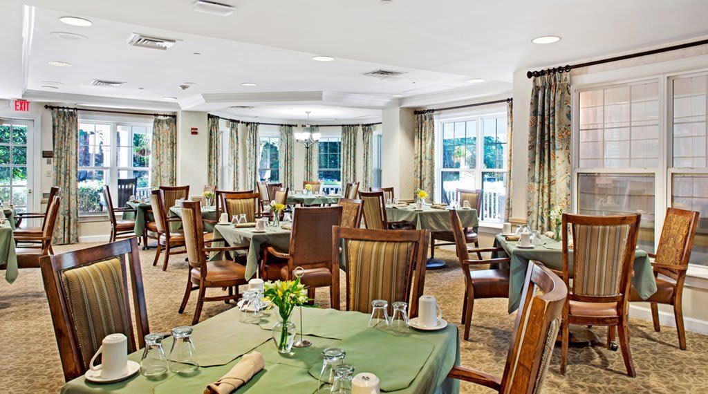 An elegant dining room with neatly arranged tables and chairs, adorned with natural light from large windows.