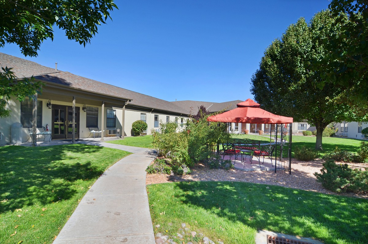 A sunny day in a landscaped area with a large building, gazebo, pathway, and green lawns.