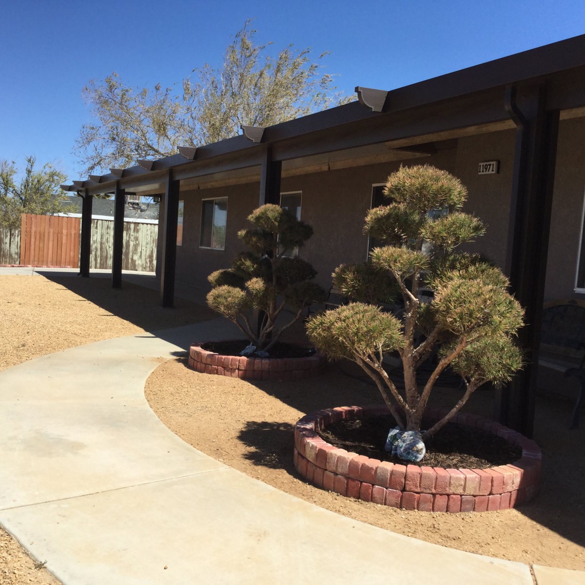 A house exterior with landscaped shrubs and a brick-bordered pathway on a sunny day.
