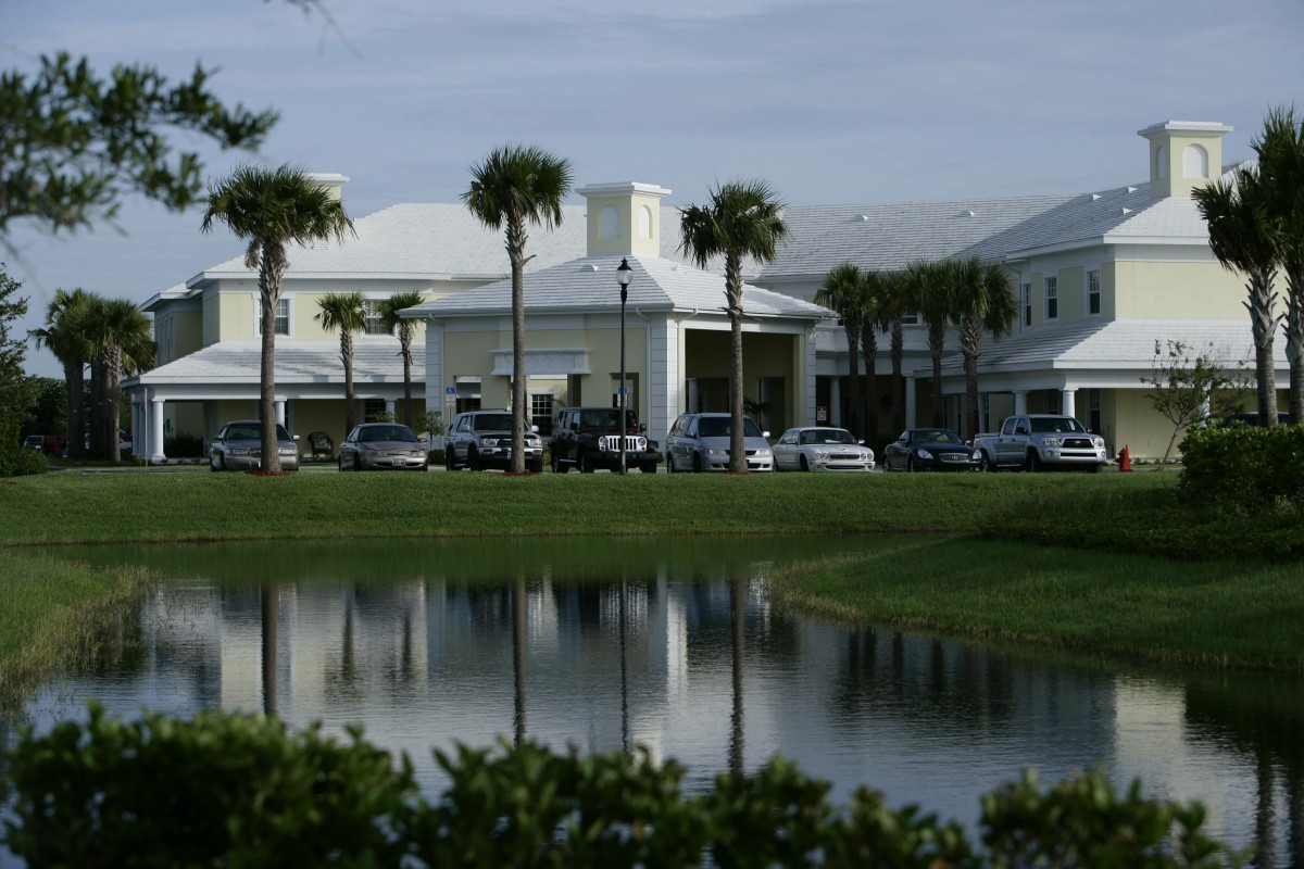 A large building surrounded by palm trees and a serene lake reflecting the scene.