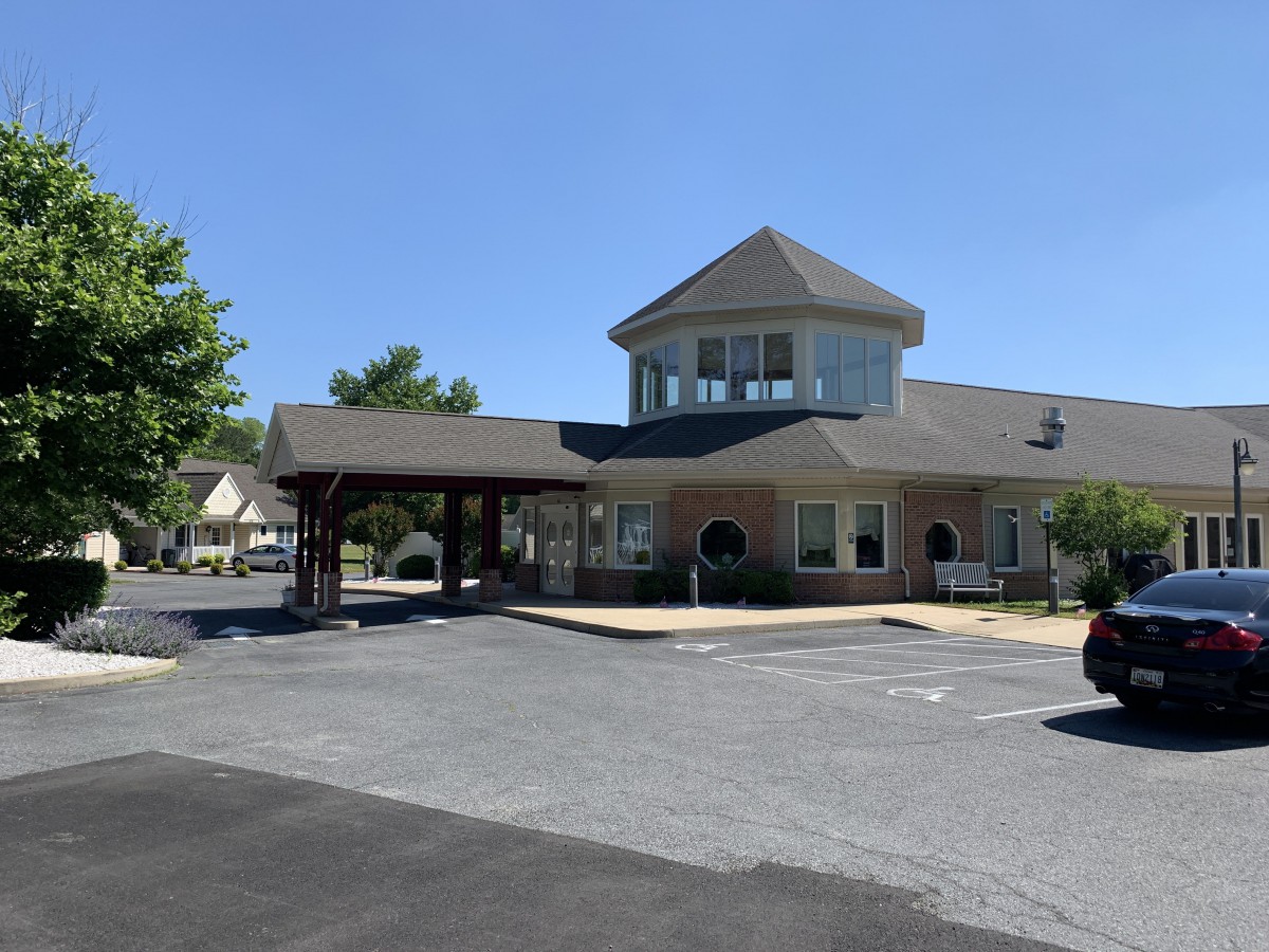 A view of a building with a covered entrance and parking lot under a clear blue sky.