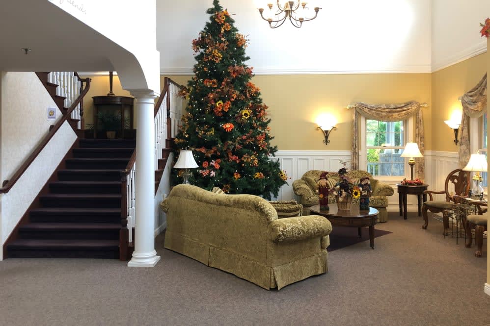 A cozy living room with a large Christmas tree decorated for the holidays, featuring a sofa and adjacent staircase.