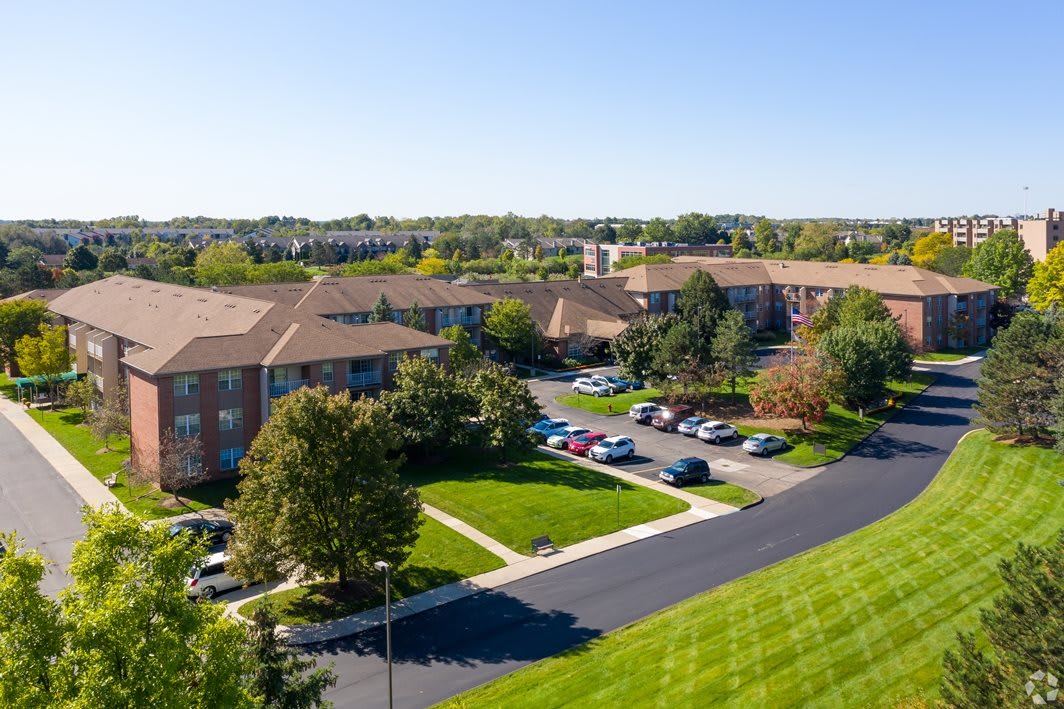 Aerial view of a suburban residential area with apartment buildings, parking lot, and lush green spaces.