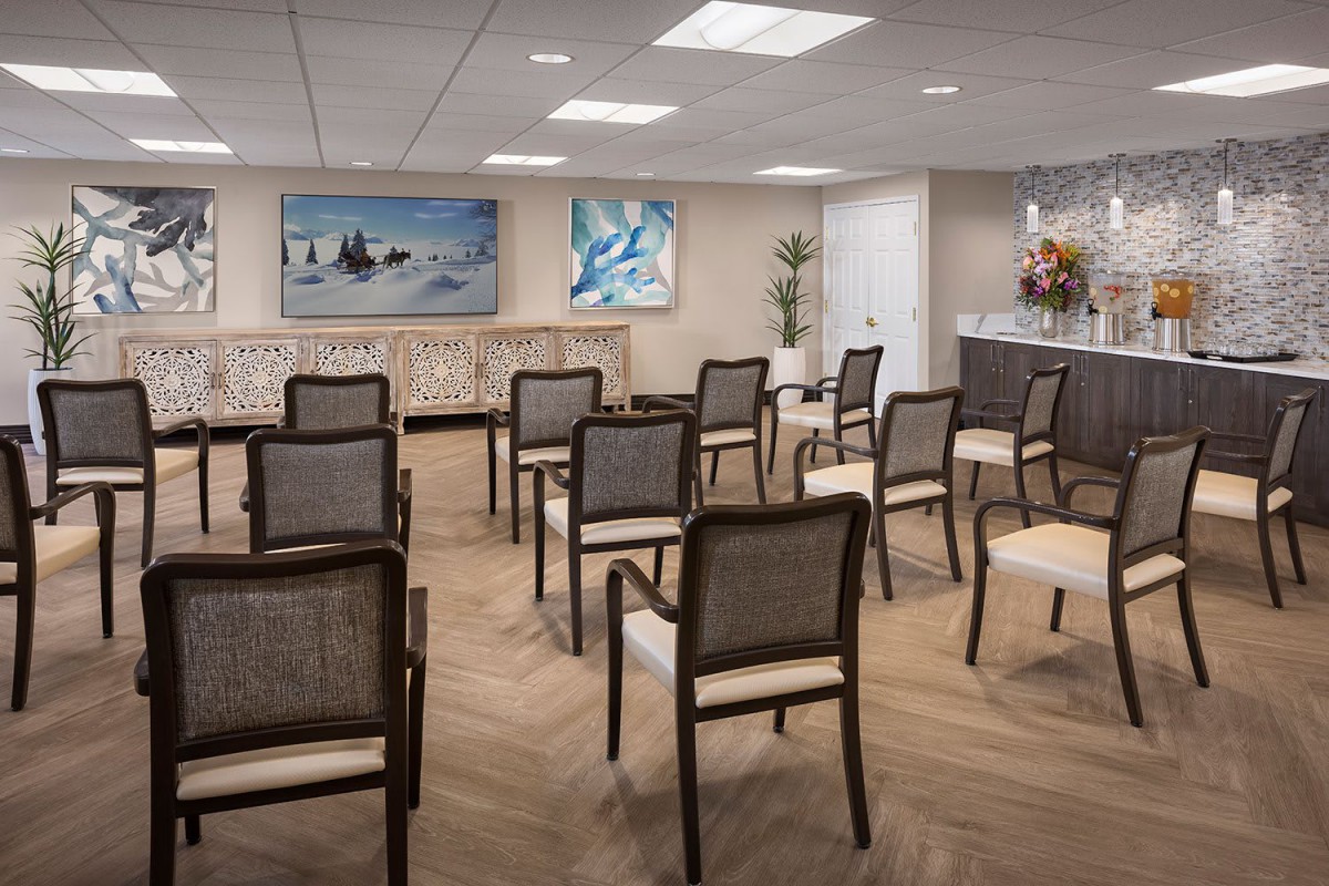 A well-organized conference room with rows of chairs facing a front desk, decorated with paintings and warm lighting.