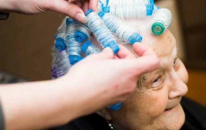 An elderly person getting their hair styled with curlers at a salon.