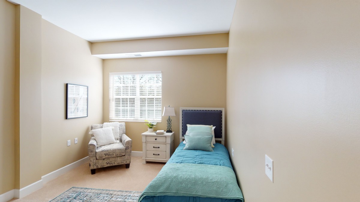 A cozy bedroom with a single bed, armchair, and nightstand by the window.