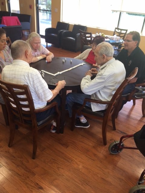 A group of seniors sitting around a table playing a game indoors.