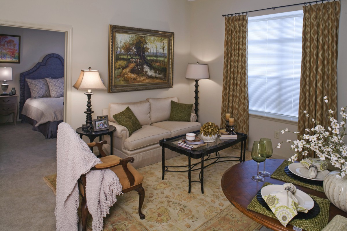 A cozy living room with elegant furniture and decor, featuring a sofa, coffee table, artwork on the wall, and warm lighting.
