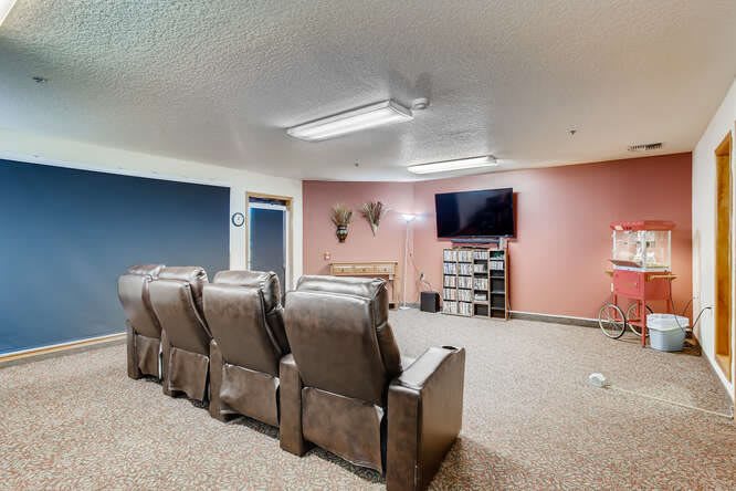 A cozy home theater setup with recliner seats facing a TV, decorated walls, and organized shelves.