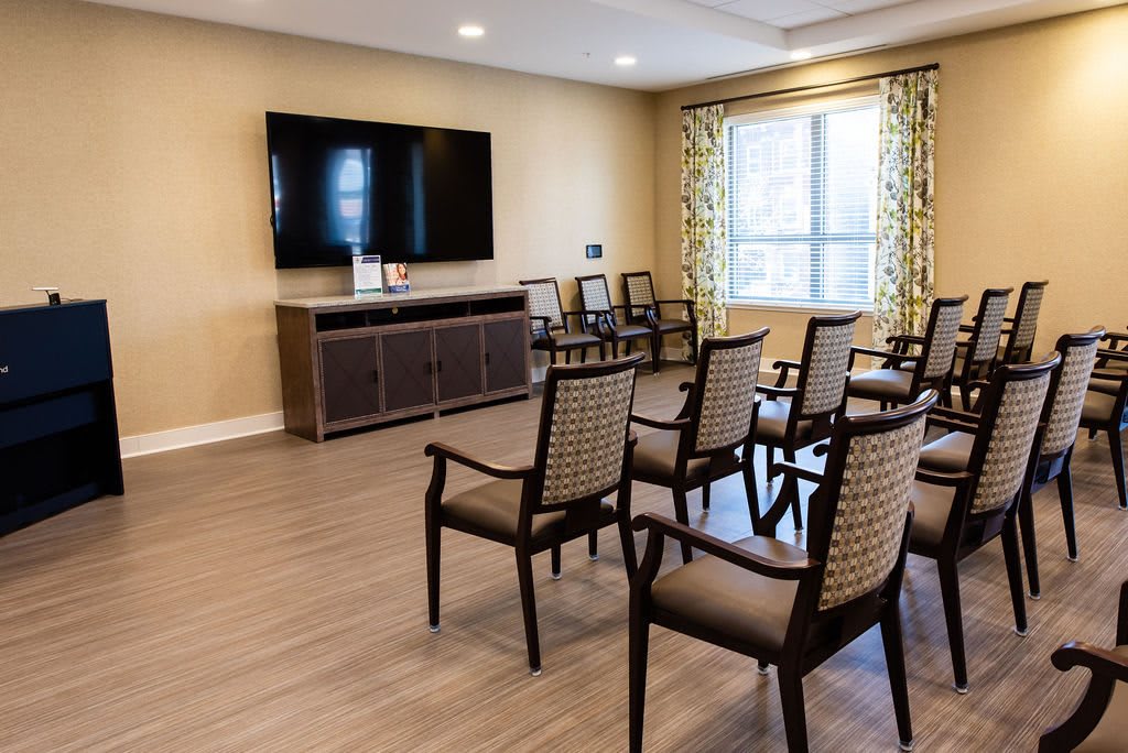 A well-lit conference room with rows of chairs facing a large television.