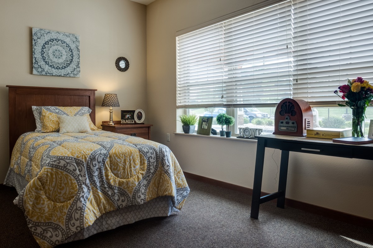 A cozy bedroom with a bed, nightstand, and window bringing in natural light.