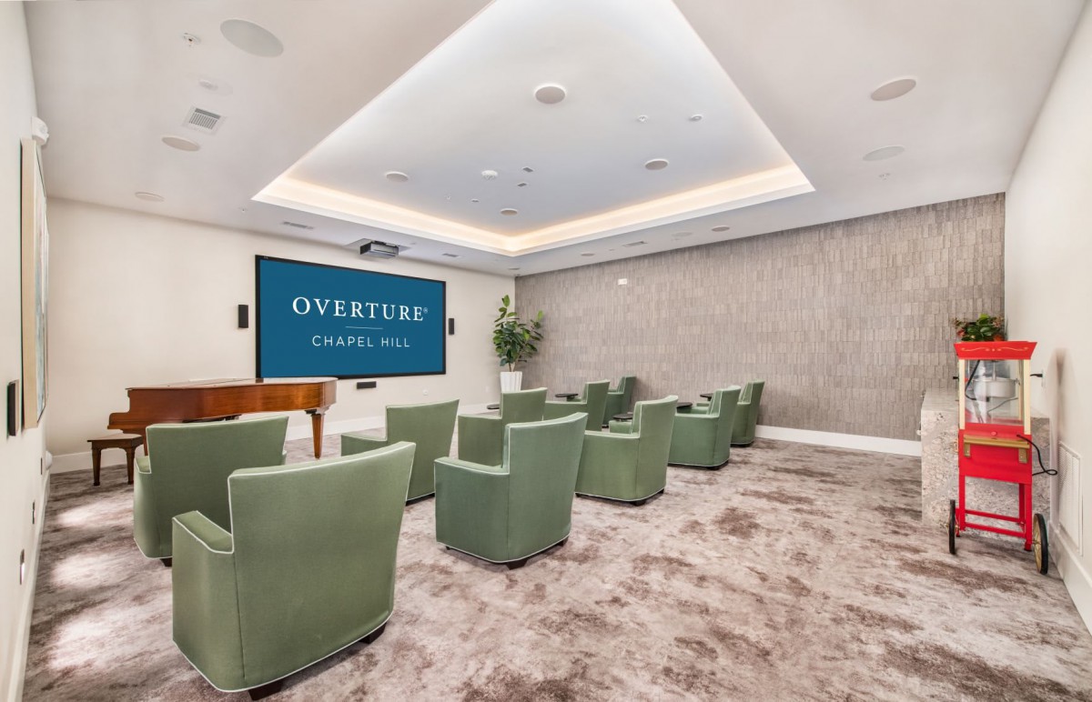A modern auditorium with green chairs facing a large screen displaying 'Overture' on the wall.