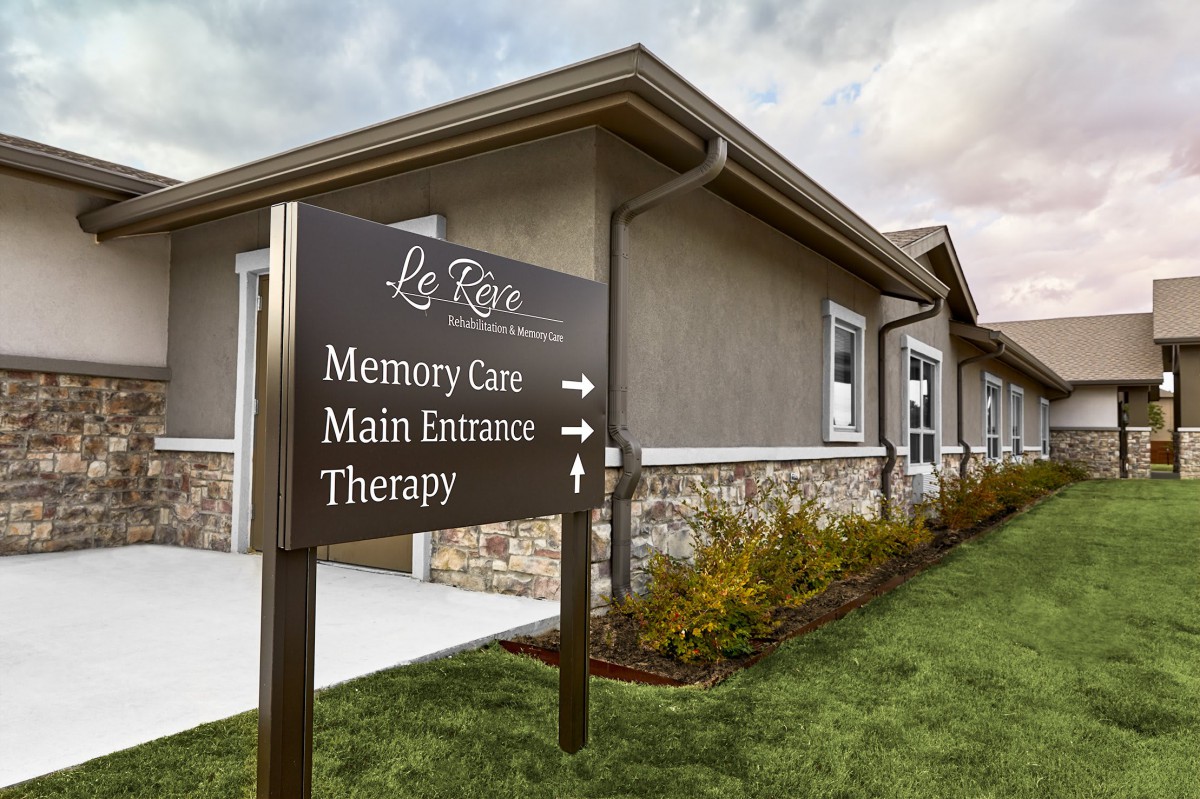 Exterior of a healthcare facility with directional signage for Memory Care, Main Entrance, and Therapy.