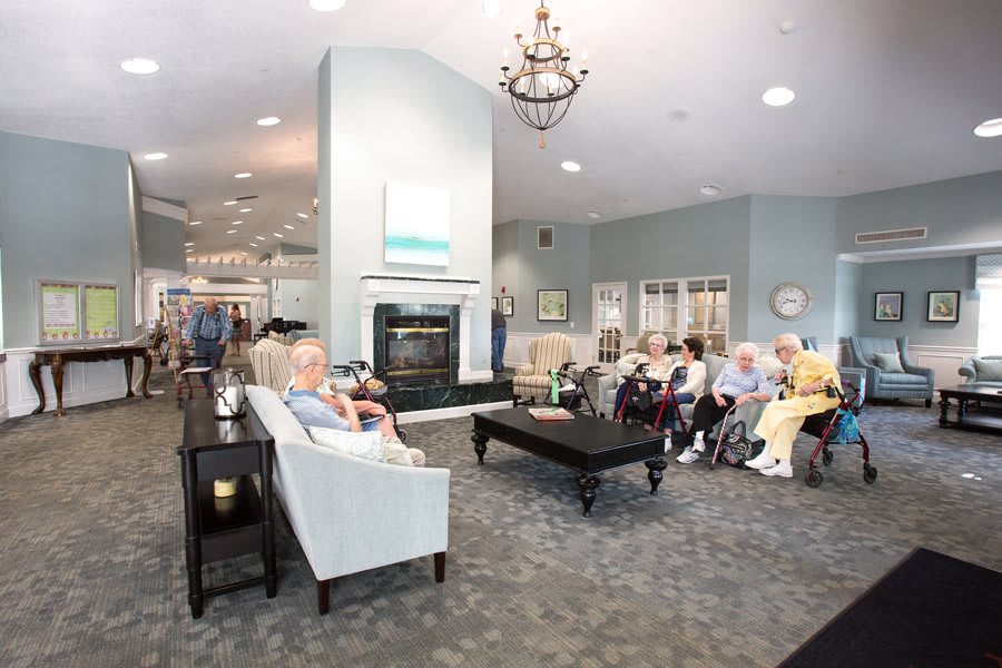 A spacious community living room with seniors seated, featuring comfortable seating and a fireplace.