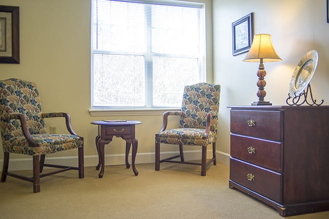 A cozy room with two chairs, a small table, and a chest of drawers by the window.