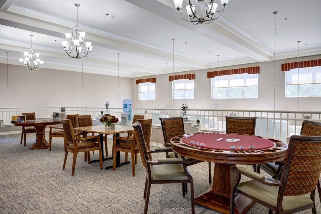 A well-lit dining area with multiple tables and chairs, adorned with chandeliers and carpet flooring.