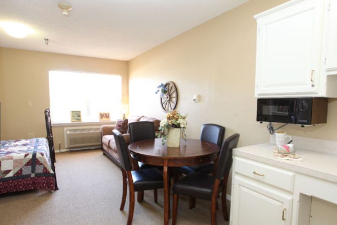 A cozy living room with a dining table and chairs, featuring ample natural light from a large window.