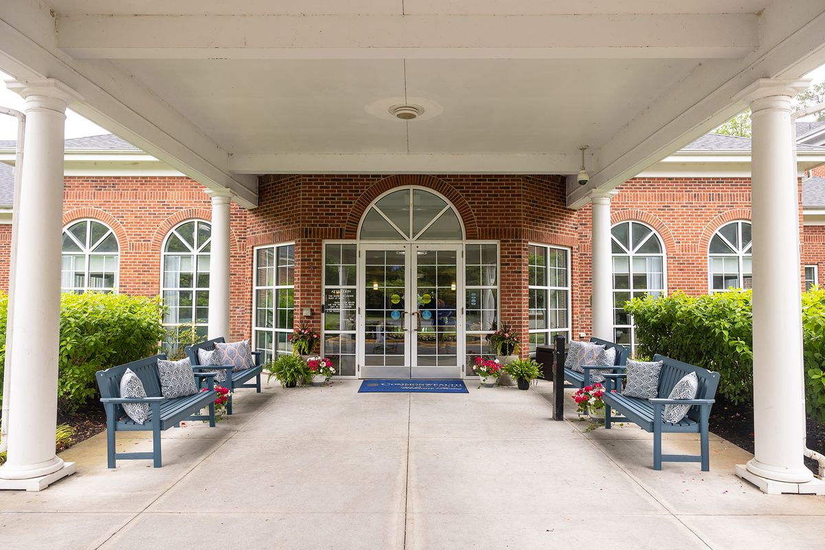 The entrance of a red brick building with a covered walkway and benches on either side.
