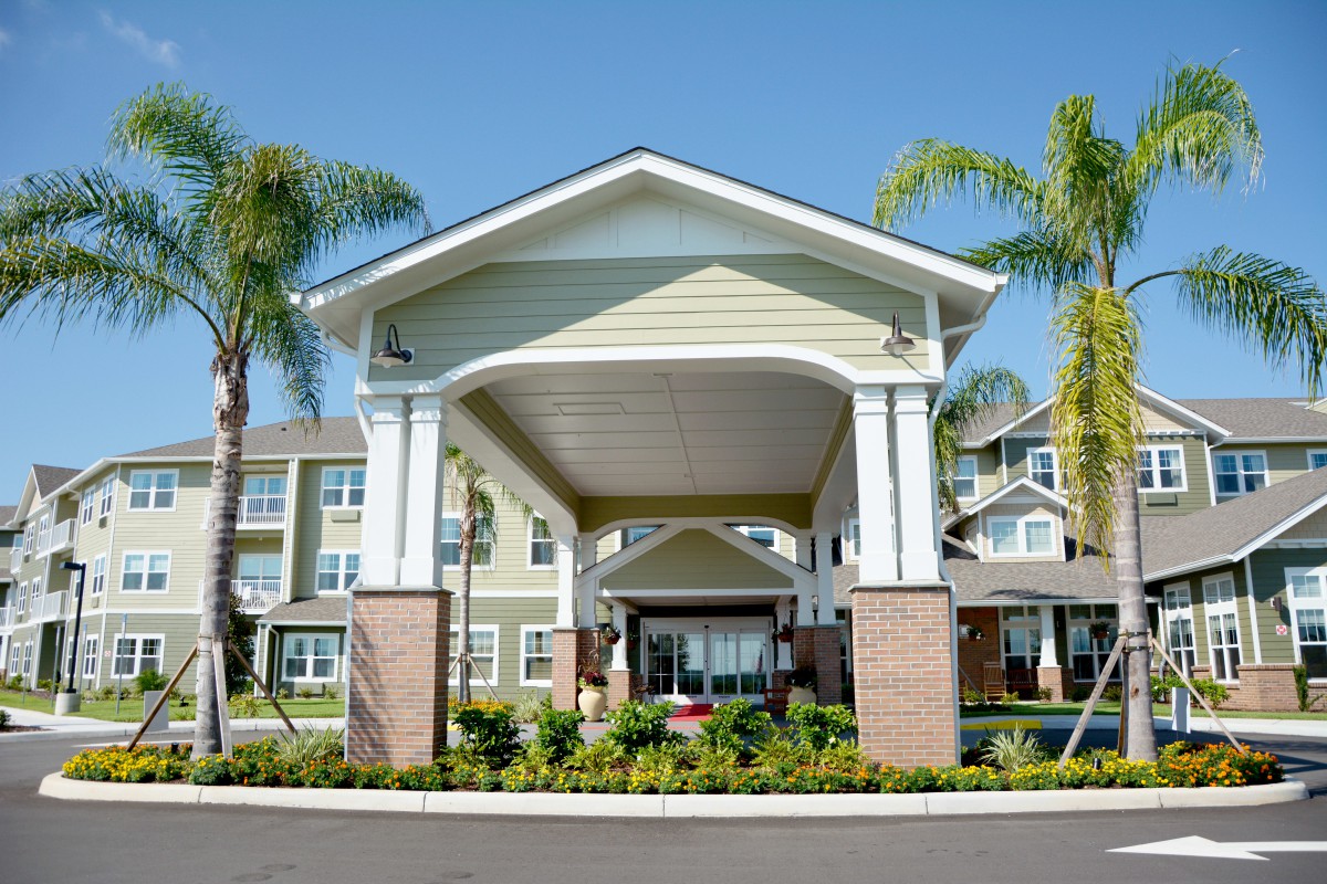 The entrance of a residential building surrounded by palm trees and well-maintained landscaping.