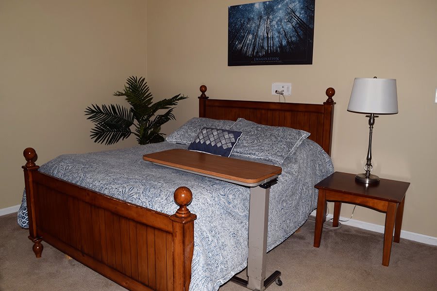 A cozy bedroom with a wooden bed, blue bedspread, and a small side table with a lamp.