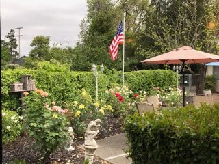 A lush garden with a variety of flowers, featuring an American flag and a cozy patio area under an umbrella.