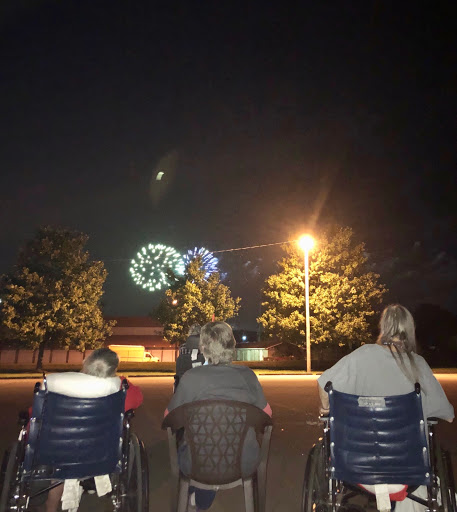 Three individuals enjoy a fireworks display under the night sky.